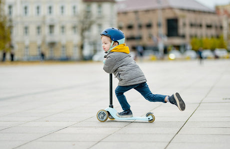 Ein kleiner Junge fährt an einem Herbsttag mit seinem Roller durch die Stadt.