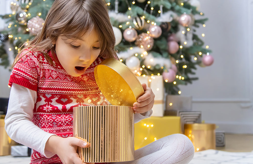 Kind öffnet Geschenke unter dem Weihnachtsbaum.