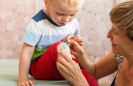 Eine Mutter klebt ein Kinderpflaster auf das Knie ihres Kindes.