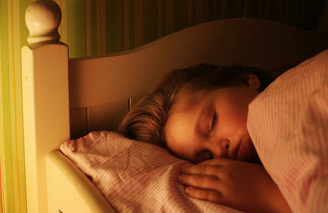 Ein Kind schläft in seinem Bett während ein Nachtlicht an ist.