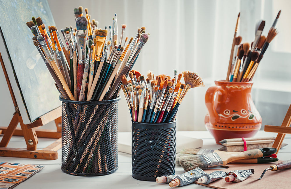 Staffelei, Pinsel, Farbtuben, Palette und Bilder auf dem Arbeitstisch in einem Künstleratelier.