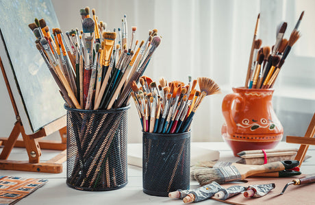 Staffelei, Pinsel, Farbtuben, Palette und Bilder auf dem Arbeitstisch in einem Künstleratelier.