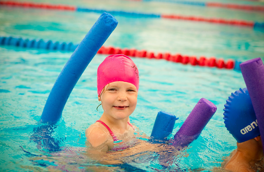Ein Kind schwimmt mit einer Schwimmnudel im Schwimmunterricht.