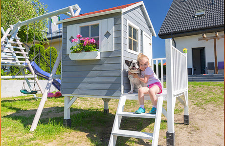 Kleines Mädchen sitzt mit ihremm Hund im Gartenspielhaus.