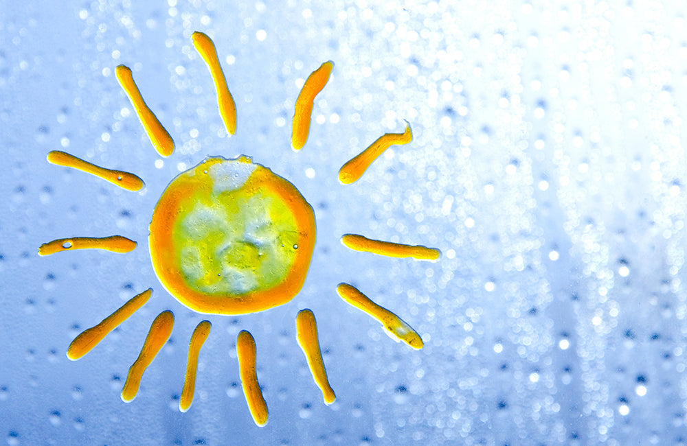 Gelbe Sonne auf einem Milchglasfenster, das mit Glasmalerei im kindlichen Stil bemalt ist.